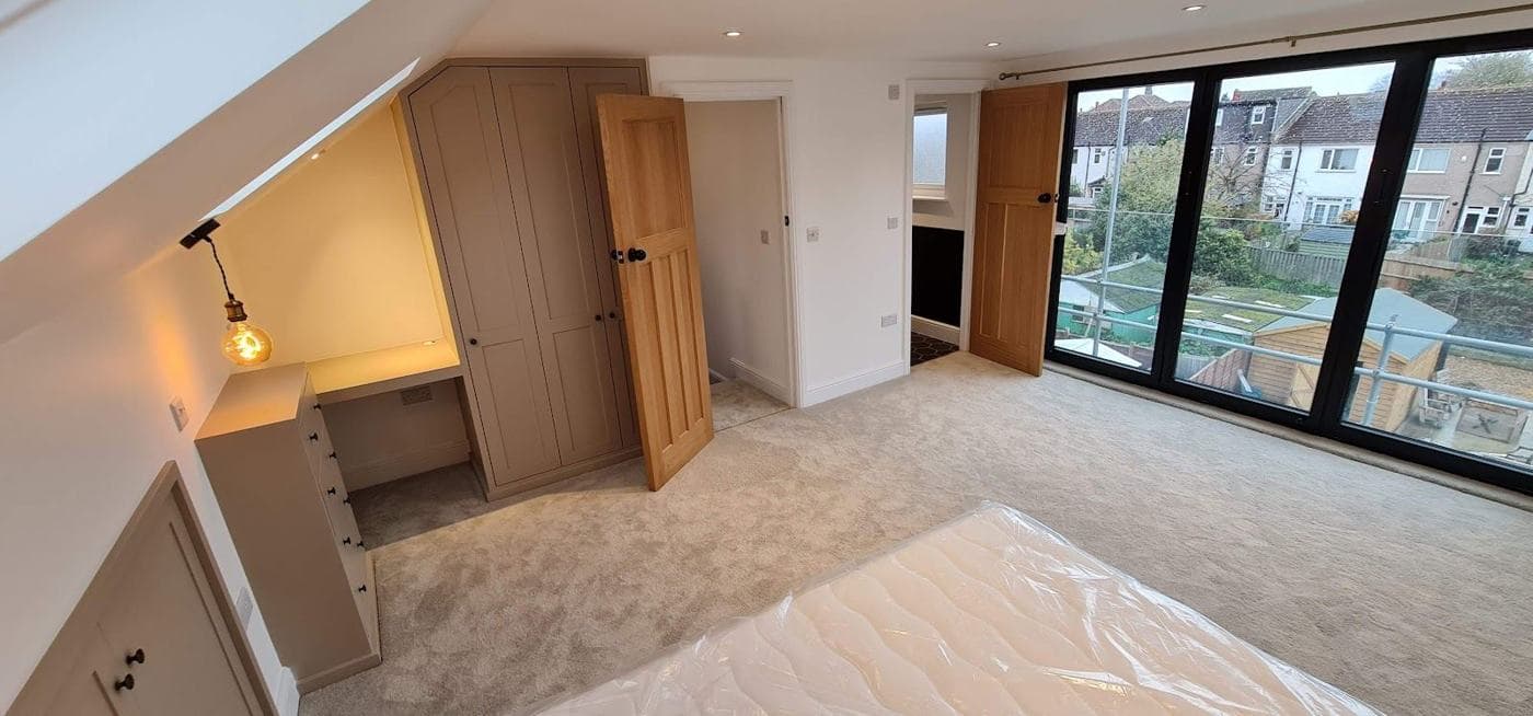 Loft conversion bedroom with rooflights, fitted storage and full-height glazing — rcbGroup project